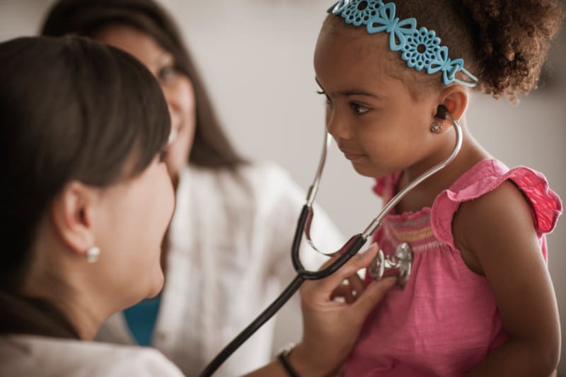 Child with doctor listening with stethoscope with parent in background