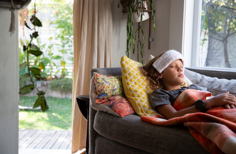 Young boy laying on couch with washcloth on forehead to soothe headache. 