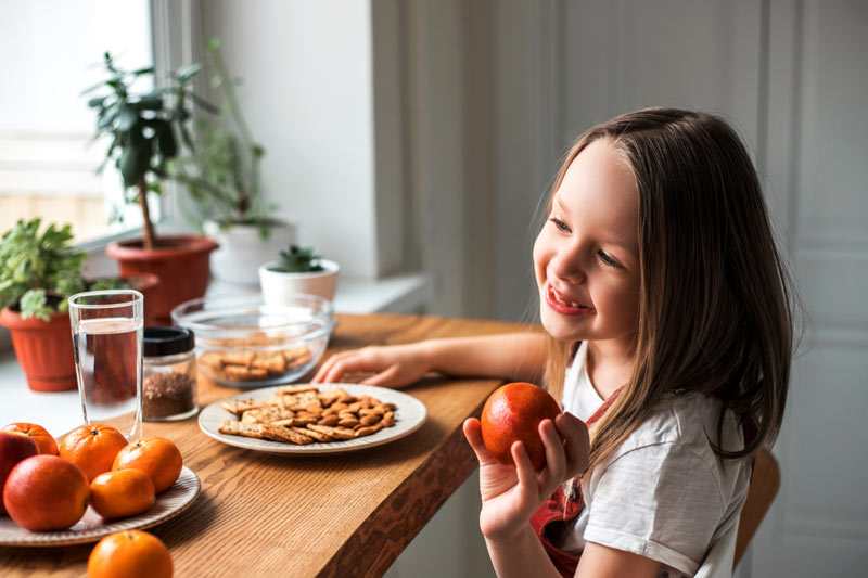 Little pretty girl eating orange and cookies at home. 