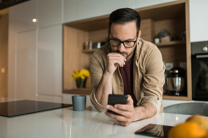 Father looking at phone in the kitchen.