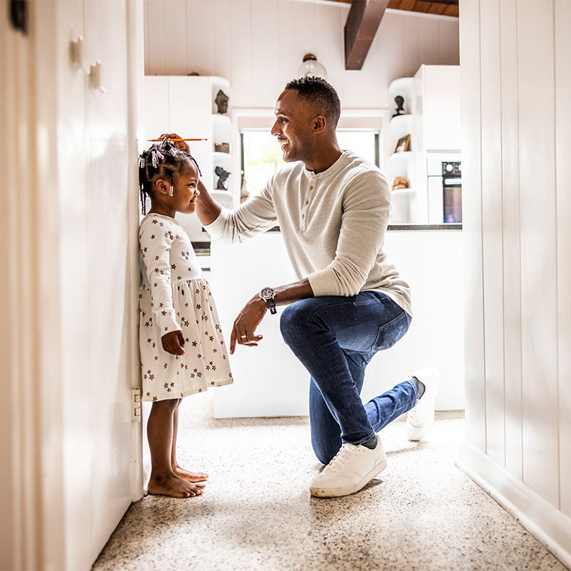 Father measuring daughter's height on wall in kitchen.