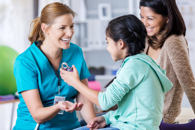 Cheerful mid adult Caucasian physical therapist encourages a young female Asian girl during session.