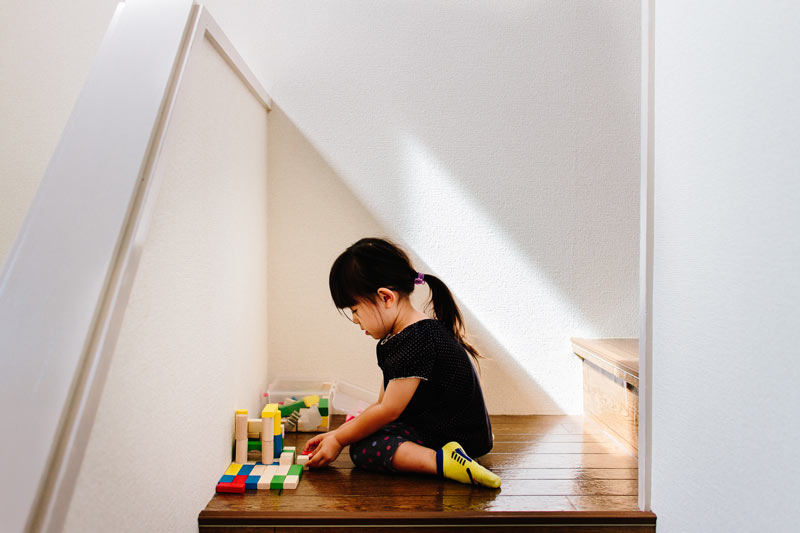 Cute little girl playing with wooden toy blocks on indoor stairs.